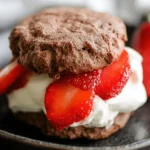 Delicious close-up of chocolate biscuits with whipped cream and fresh strawberries on a dark plate.