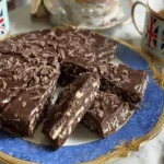 Elegant chocolate biscuits cake served on a luxurious gold and blue plate with British-themed tea cups.