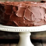 Decadent multi-layered chocolate cake with rich dark frosting on an elegant white cake stand.