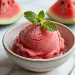 A bowl of vibrant watermelon sorbet served with fresh mint leaves.