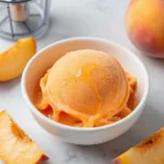 A bowl of homemade peach sorbet served with fresh peach slices.