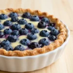 A baked dish featuring cottage cheese, blueberries, and a golden crust, served in a white ceramic dish.