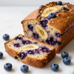 A freshly baked loaf of oatmeal blueberry banana bread on a wooden table.