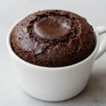 A freshly made Oreo mug cake served in a white mug on a wooden table.