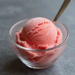 A bowl of vibrant pink watermelon sorbet garnished with fresh mint leaves.