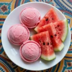 A bowl of vibrant pink watermelon sherbet made using the Ninja Creami machine, garnished with fresh mint leaves.