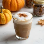 A homemade iced pumpkin cream chai latte served in a glass with a straw on a wooden table.