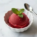 A bowl of vibrant homemade watermelon sorbet served with fresh mint leaves.