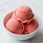 A bowl of vibrant pink watermelon sorbet garnished with fresh mint leaves.