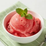 A bowl of vibrant pink watermelon sorbet served with fresh mint leaves.