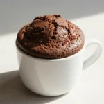 A freshly baked keto mug cake served in a white ceramic mug on a wooden table.