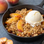 A freshly baked peach crisp in a white baking dish with a golden brown crumbly topping.