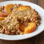 A freshly baked healthy peach crumble served in a white dish.