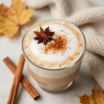 A warm autumn spice latte topped with frothy milk and a sprinkle of cinnamon, served in a cozy ceramic mug.
