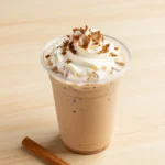 A glass mug filled with pumpkin chai tea topped with creamy cold foam on a wooden table.