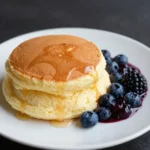 A stack of fluffy Japanese soufflé pancakes topped with powdered sugar and fresh strawberries.