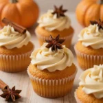 Freshly baked pumpkin cupcakes topped with cream cheese frosting on a wooden table.