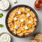 A bowl of creamy Crockpot Buffalo Chicken Dip topped with chopped green onions and served with celery sticks and tortilla chips