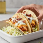 Cheesy oven-crispy chicken bacon ranch tacos topped with melted cheese and fresh herbs on a serving plate