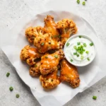 A bowl of crispy buffalo cauliflower wings served with ranch dip and celery sticks