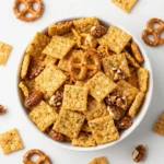 A bowl of ranch trail mix snack mix with pretzels, nuts, crackers, and seasoned bites on a rustic table.