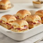 Baked ham and cheese sliders on a baking tray with melted cheese and golden-brown tops