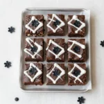 Fudgy Halloween brownies decorated with orange and black icing, candy eyes, and festive sprinkles on a dark tray