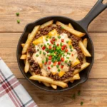 A plate of Cajun dirty loaded fries topped with seasoned ground meat, melted cheese, green onions, and a drizzle of creamy sauce.