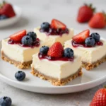 Patriotic no-bake flag cheesecake bars topped with strawberries and blueberries on a serving platter