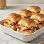 Baked ham and cheese sliders stacked in a pan with melted cheese and buttery tops