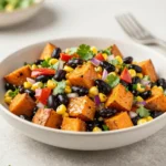 A bowl of roasted sweet potato black bean salad with greens, corn, avocado, and a light dressing