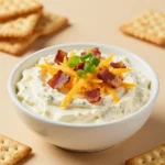 A creamy crack dip served in a bowl with crackers and sliced vegetables on a serving platter.
