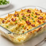 A creamy loaded baked potato casserole topped with melted cheese, crispy bacon, sour cream, and chopped green onions in a baking dish.