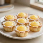 Delicate flower tarts topped with colorful edible petals and fresh fruit on a white serving plate.