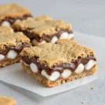Stacked s'mores cookie bars with gooey marshmallow, melted chocolate, and a graham cracker cookie crust on a white plate.