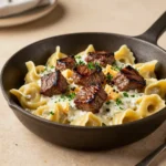 A bowl of garlic steak tortellini topped with sliced seared steak, creamy sauce, and chopped parsley.