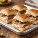 Close-up of hot Italian sub sliders topped with melted cheese, sliced meats, and toasted buns on a serving platter