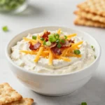 A creamy crack dip served in a bowl with a spoon and crackers on the side