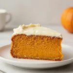 A frosted pumpkin cake topped with cinnamon dust and pumpkin spice decor on a rustic table