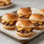 Tray of easy cheeseburger sliders with melted cheese, sesame seed buns, lettuce, and pickles on a baking sheet