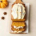 Slice of pumpkin bread topped with creamy cream cheese frosting on a white plate