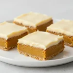 A tray of keto pumpkin bars topped with creamy cream cheese frosting and a light dusting of cinnamon.