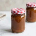 A glass bottle of pumpkin spice syrup surrounded by cinnamon sticks, star anise, and slices of pumpkin on a wooden table.