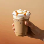 A mug of pumpkin cinnamon roll latte topped with whipped cream, cinnamon, and a swirl of caramel on a cozy table