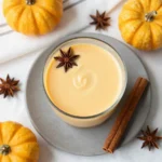 A creamy glass of pumpkin spice milk topped with cinnamon on a wooden table