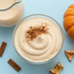 A creamy pumpkin cold foam topped on an iced coffee in a clear glass with autumn spices nearby